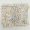 A square knitted fabric swatch in a cream or off-white color, featuring a textured knit pattern with scattered iridescent sequins that reflect multiple colors, set against a plain white background.
